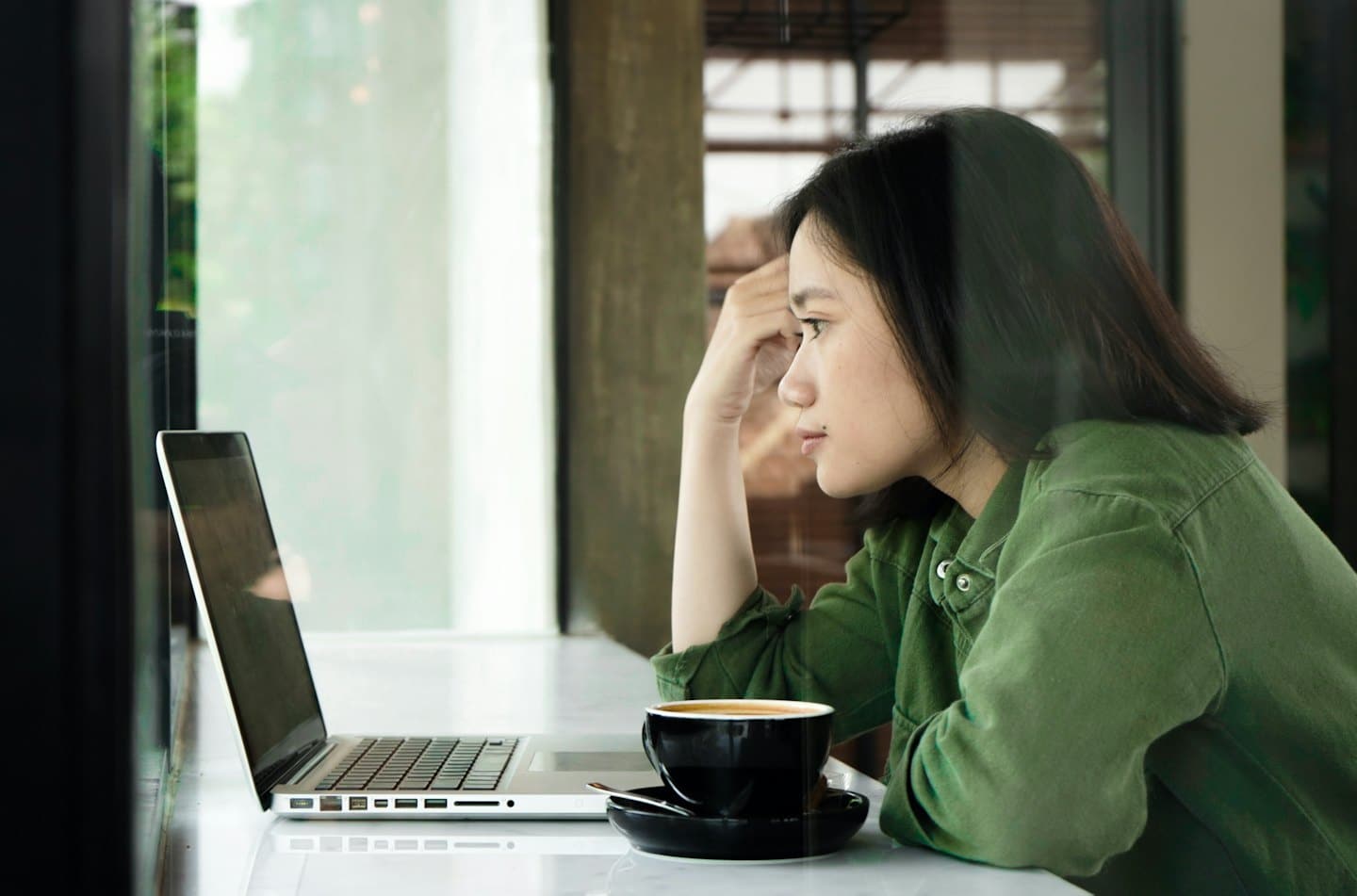 Woman in a green shirt sits at a desk working remotely.